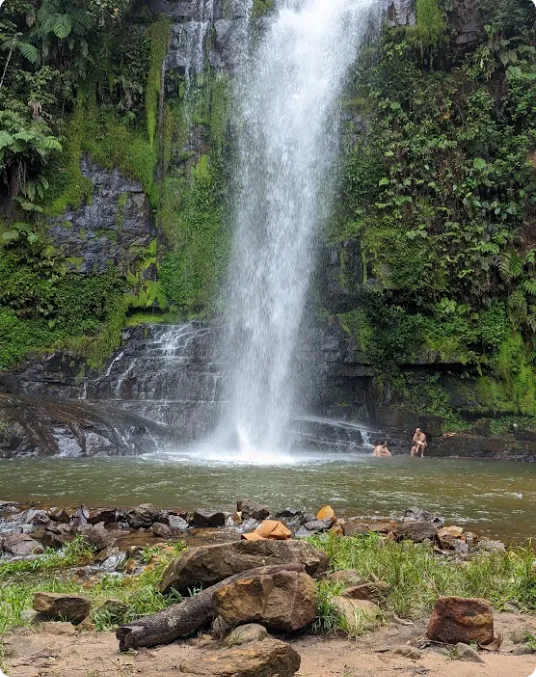 cachoeira pé da serra, duas pessoas estão nas pedras bem do lado da queda de água da cachoeira.