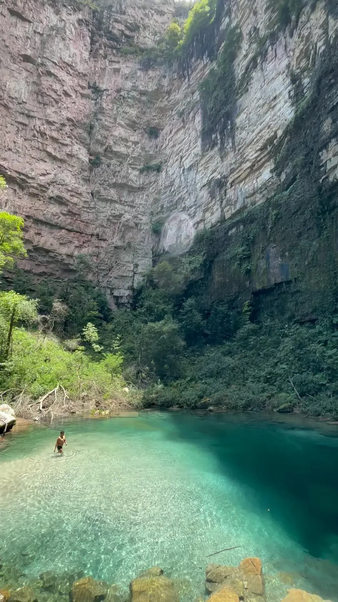 vista horizonta do santuario das araras, o sol mais o paredão de pedra está criando uma sombra na metade dá aágua, uma pessoa está entrando na água.