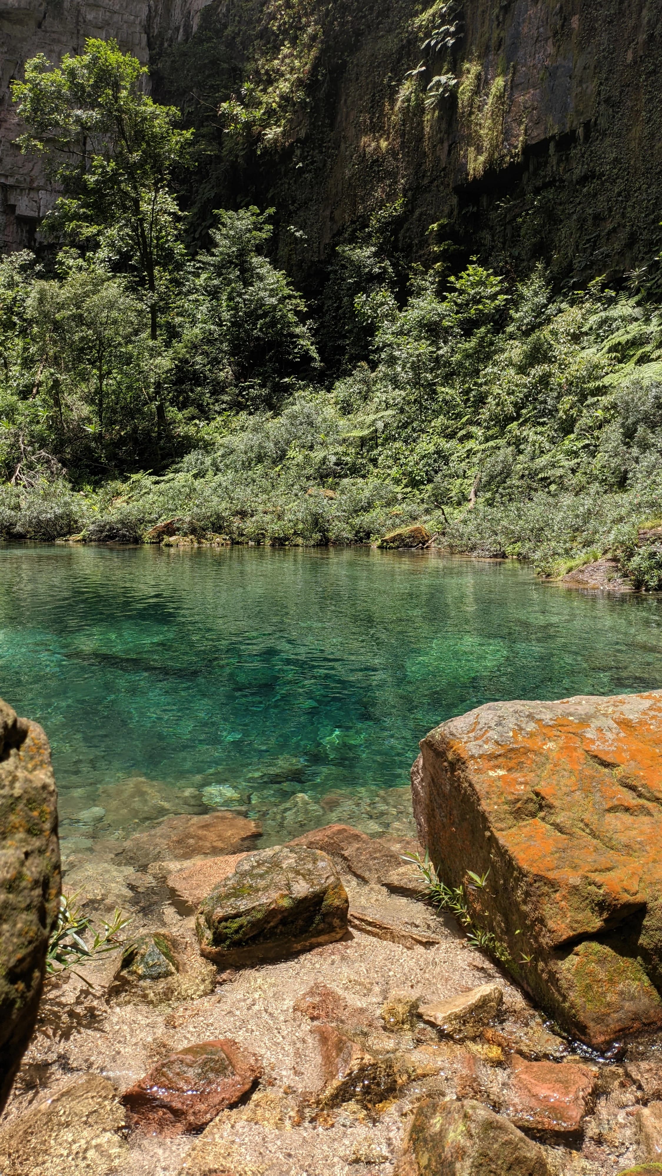 vista vertical do santuario das araras com a agua de tonalidade azulada e algumas rochas com um musgo laranja por cima