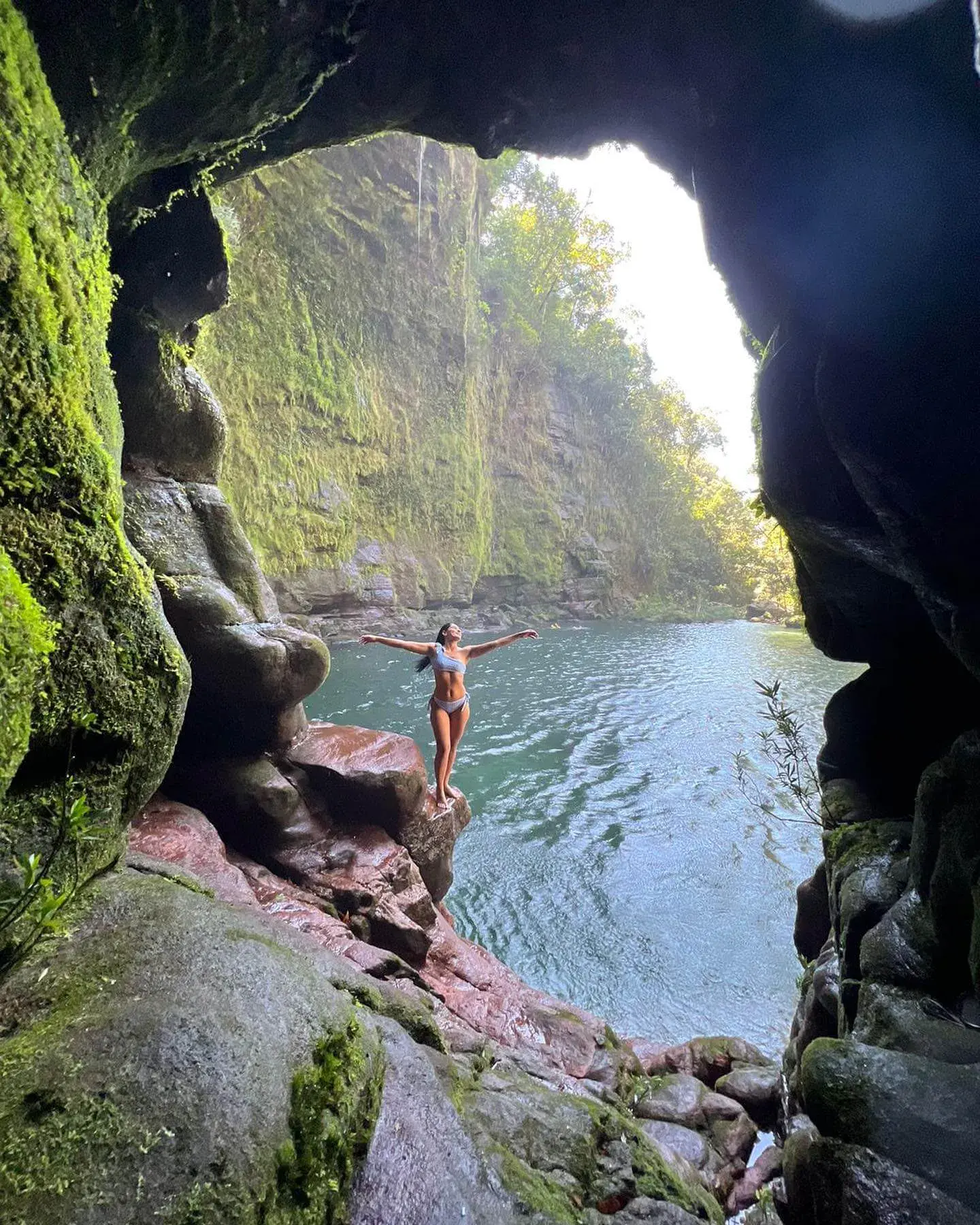 uma mulher tirando foto de dentro da caverna e de fundo tem o poço da cachoeira azul