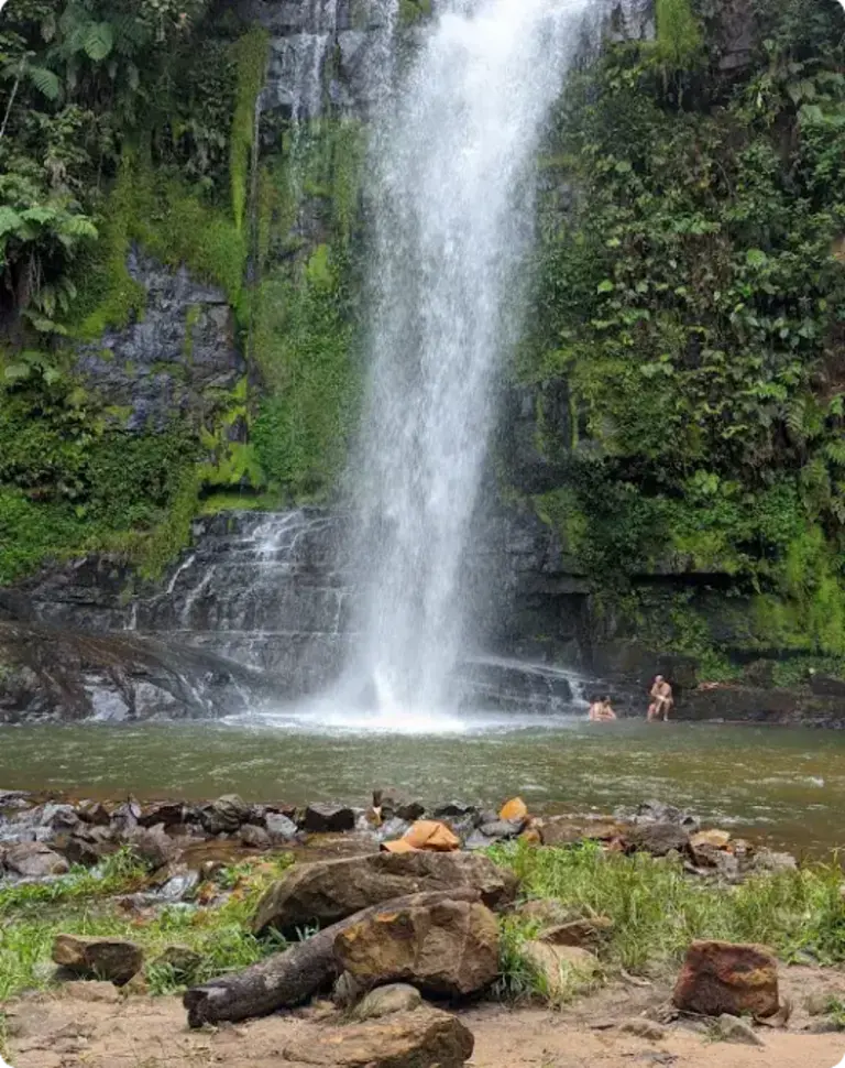 Visitantes desfrutando da Cachoeira Pé da Serra, posicionados nas pedras próximas à queda d'água.