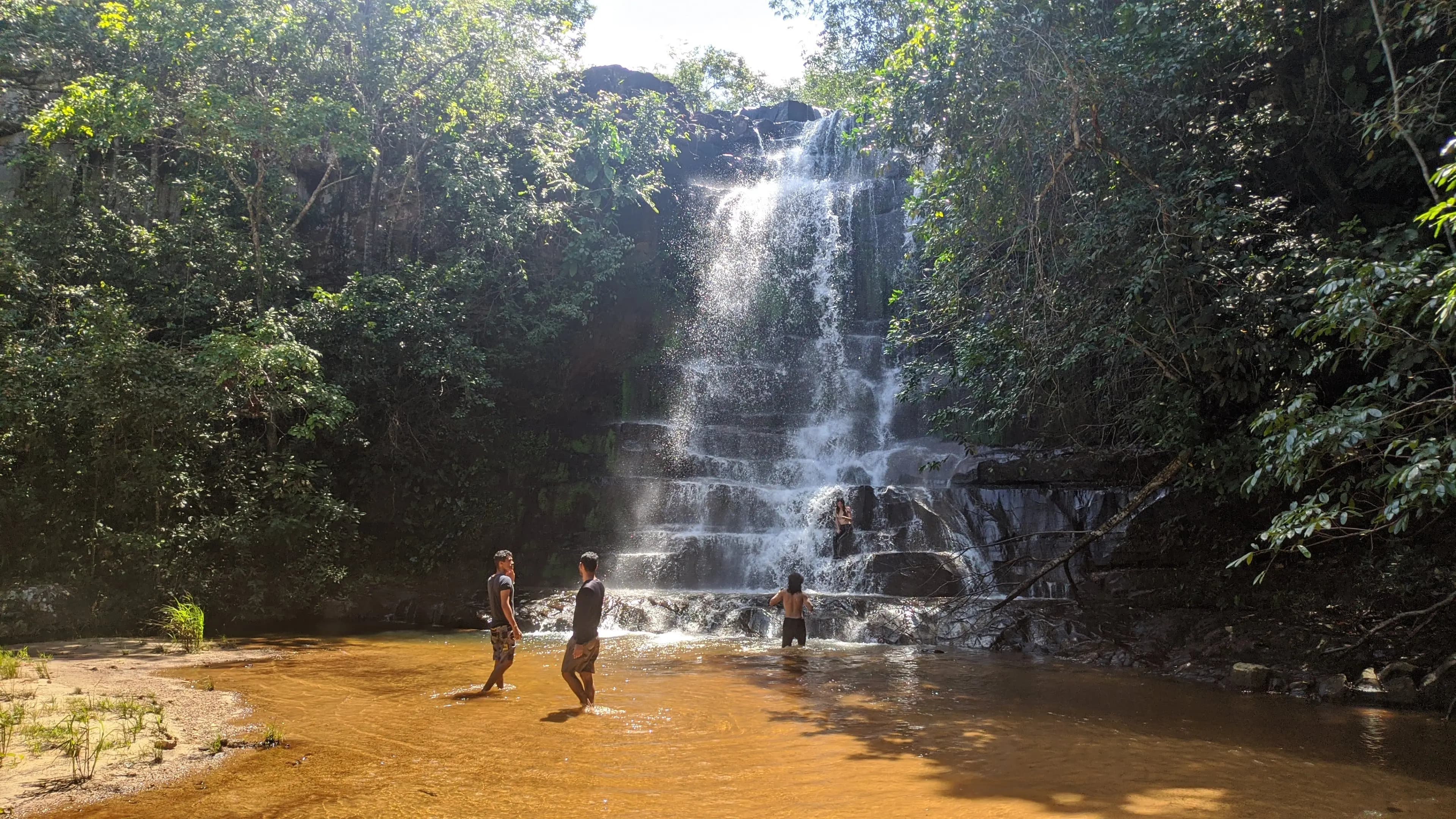 Visitantes se refrescando em uma das cachoeiras da trilha com queda d'água de aproximadamente 5 metros e formações rochosas em degraus naturais